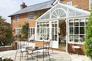 An elegant conservatory attached to a brick house, with outdoor seating on a patio